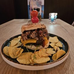 Hamburger Kade 6, bestaat uit een huisgemaakte hamburger, met pulled pork van de barbecue. Op een vers sesambroodje met sla, tomaat, cheddar en augurkenrelish. smullen maar